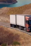 A Renault Trucks T tractor-trailer is traveling along a winding road overlooking a mountain lake.